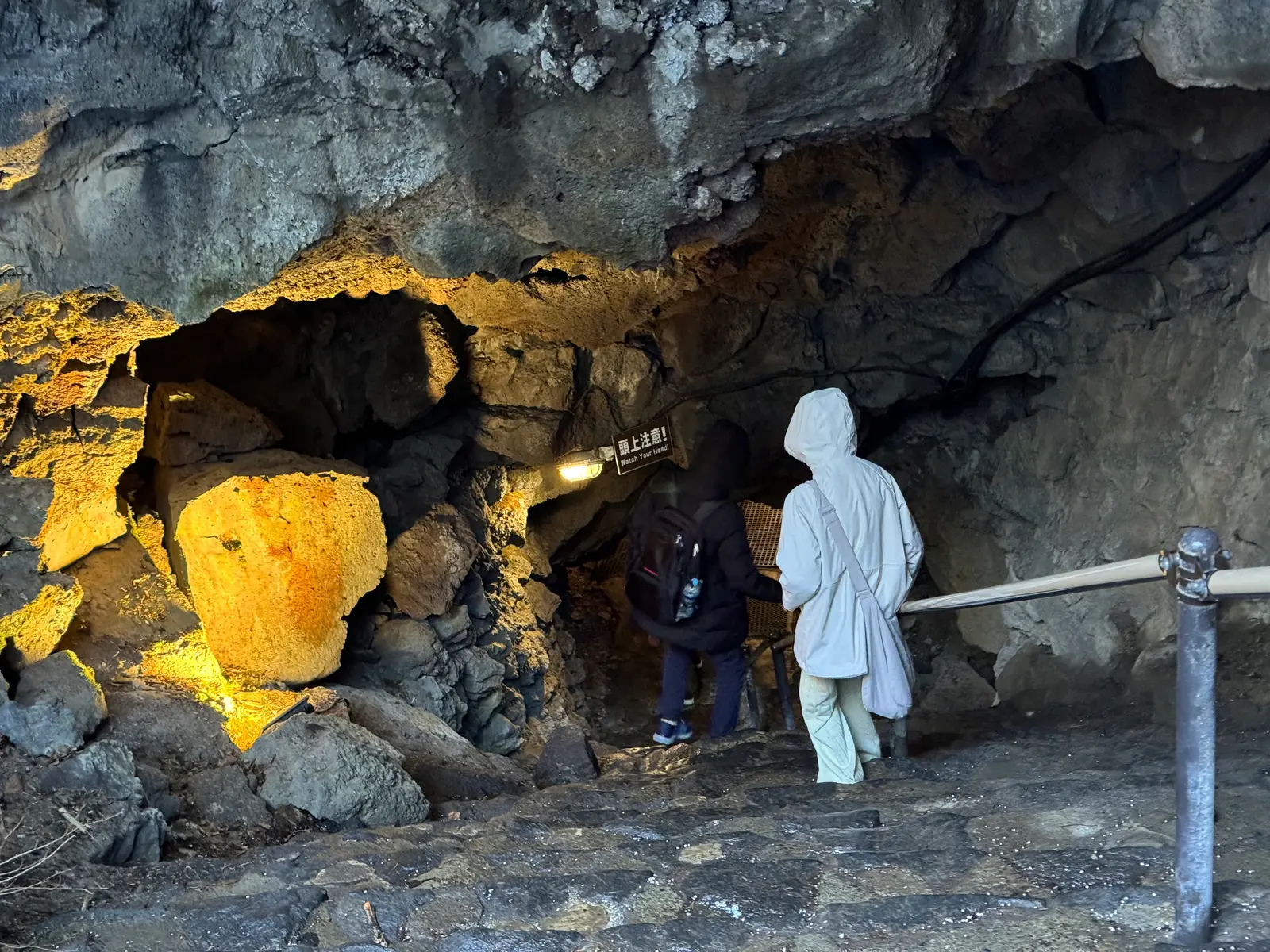 Visitors walking through a lit lava cave with a stone path and railing