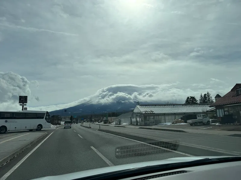 Mount Fuji under a cap of clouds above a road and greenhouses near Kawaguchiko