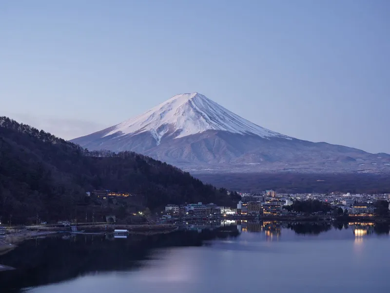 Snow-capped Mt Fuji at dusk above Lake Kawaguchi, lights coming on in the lakeside town