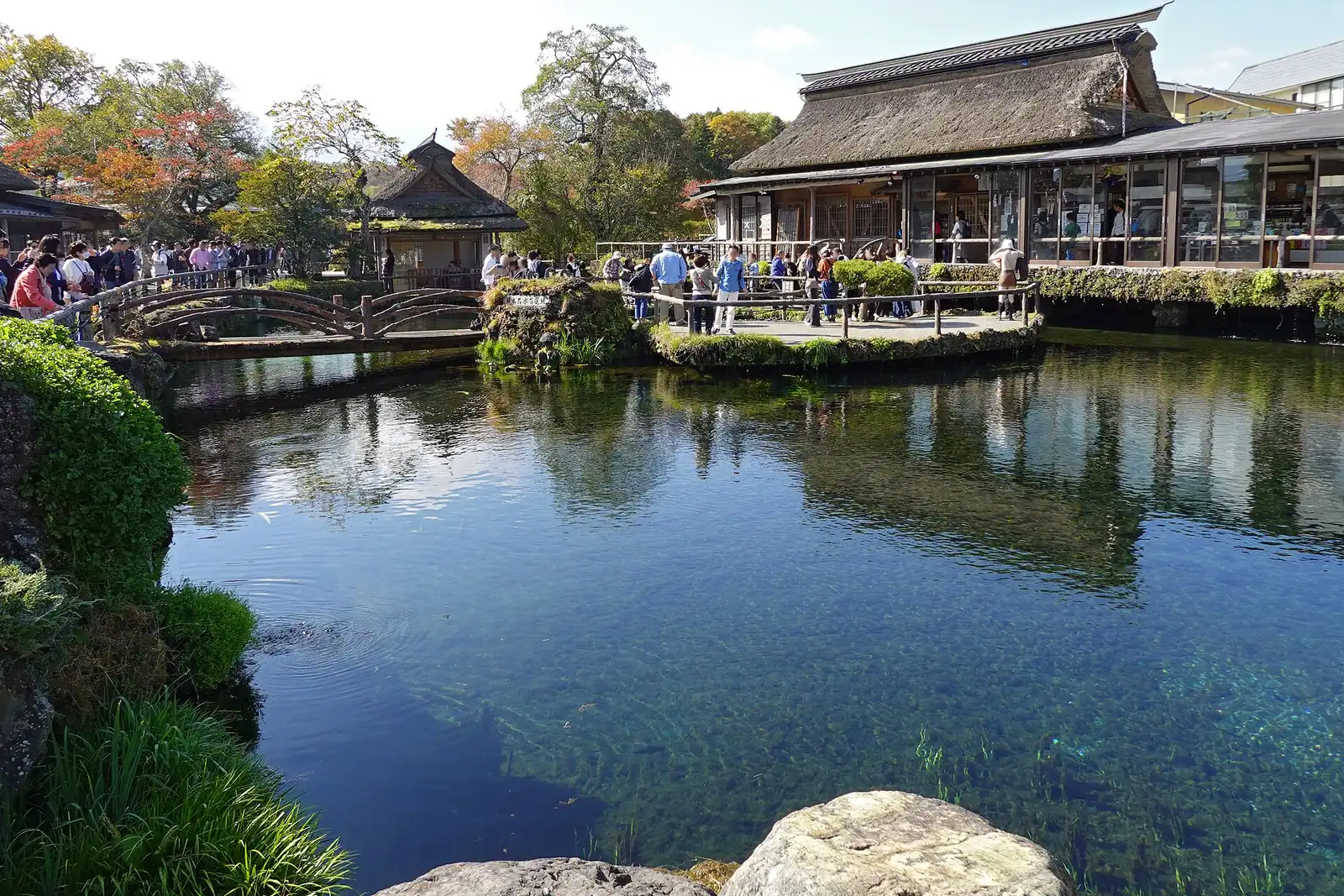 Spring pond at Oshino Hakkai with a wooden bridge and thatched house, autumn trees